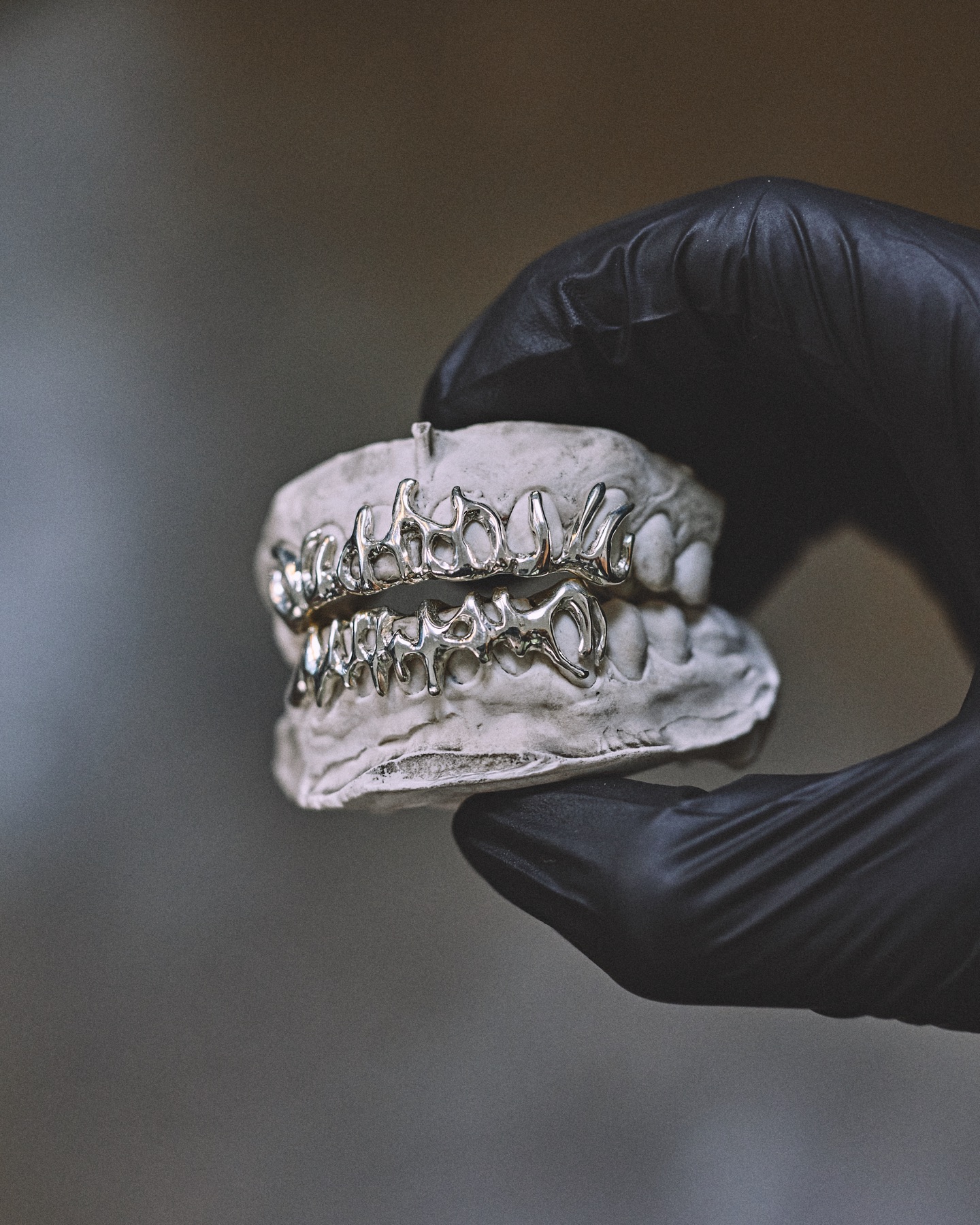Main gantée tenant un grillz en argent au-dessus d'un moulage dentaire