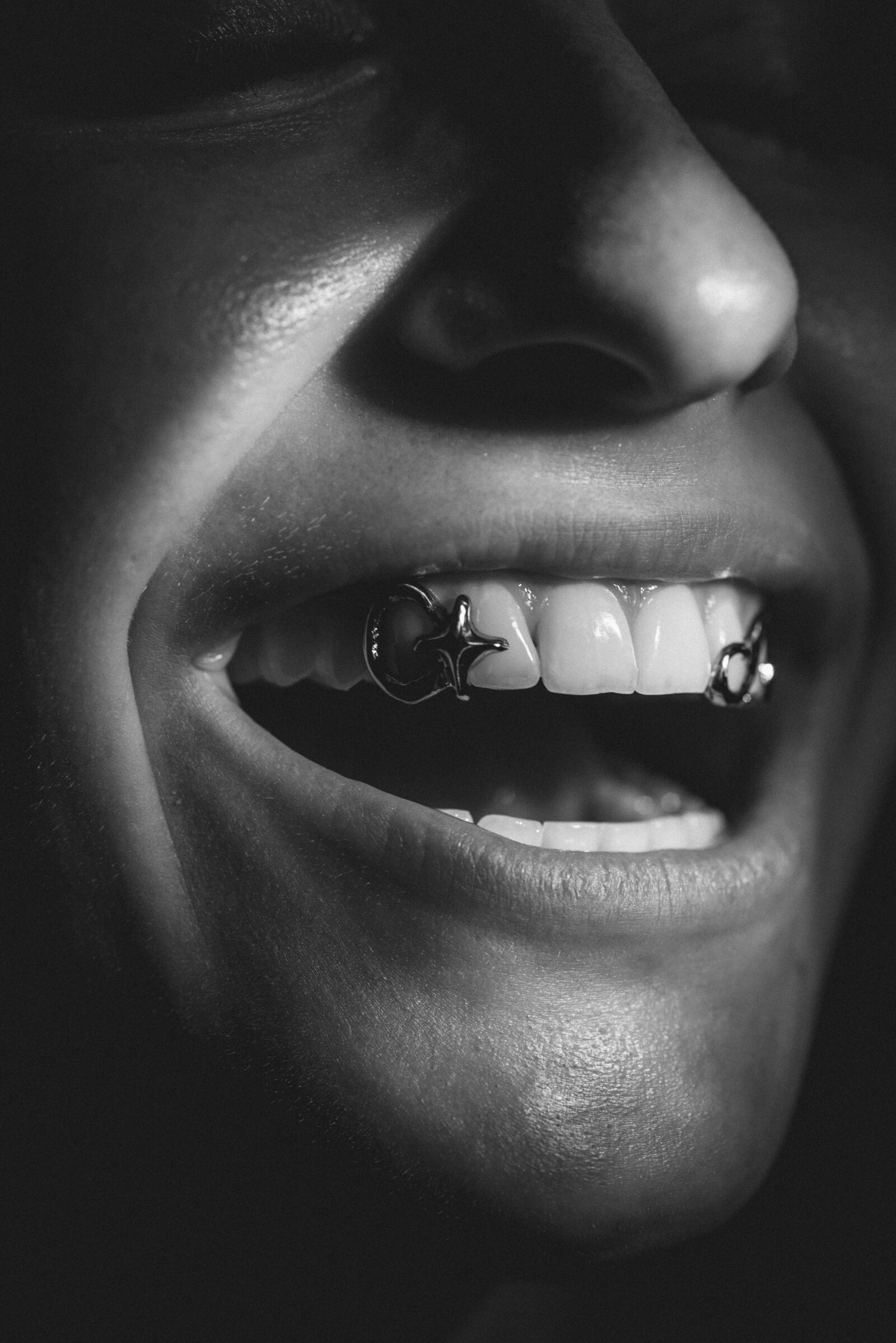 Sourire portant deux grillz sculptés en argent, portrait noir et blanc aux ombres douces